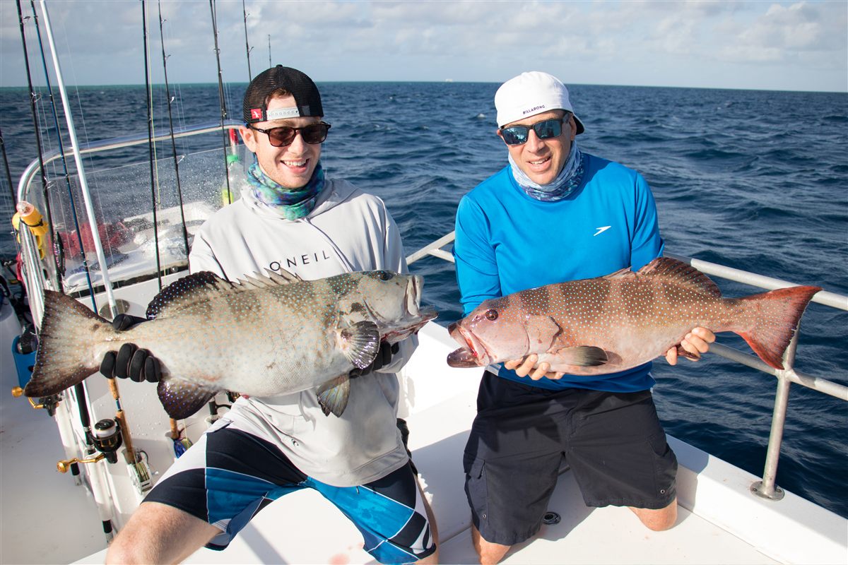 Will and Michael holding coral trout on a boat at the Great Barrier Reef