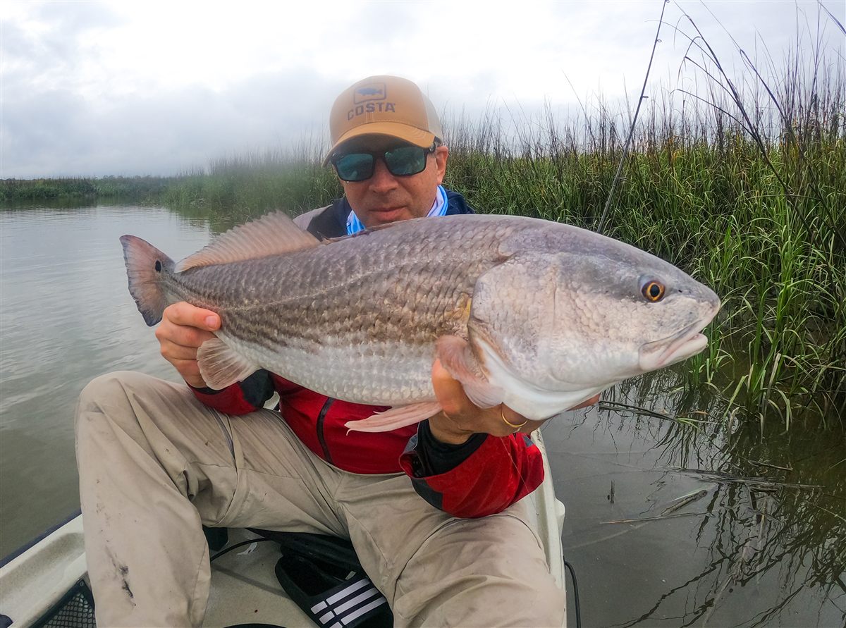 Michael holding a redfish among the marsh grass in Sea Island